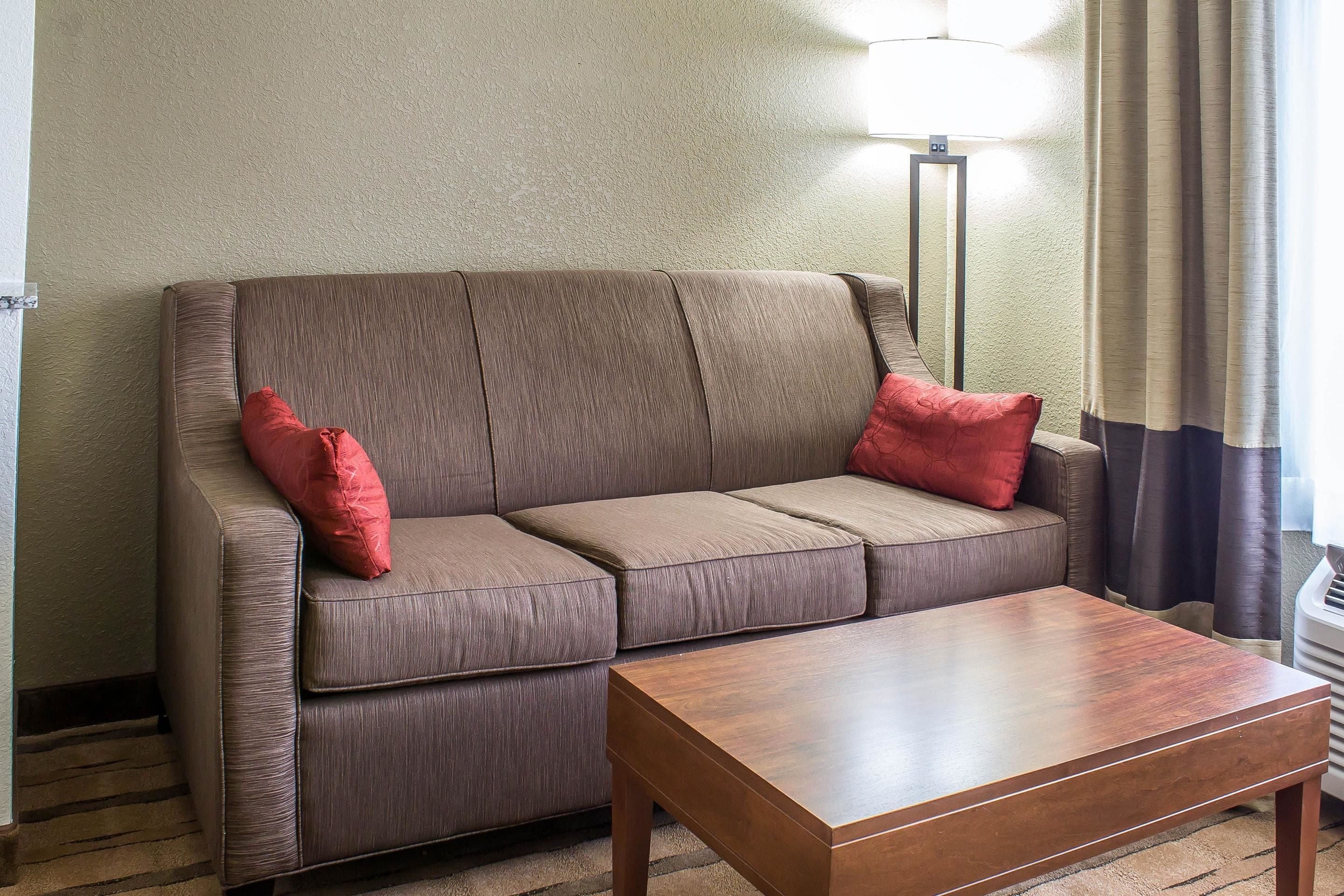 A brown sofa with two red pillows and a wooden coffee table in a room with a lamp and curtains.