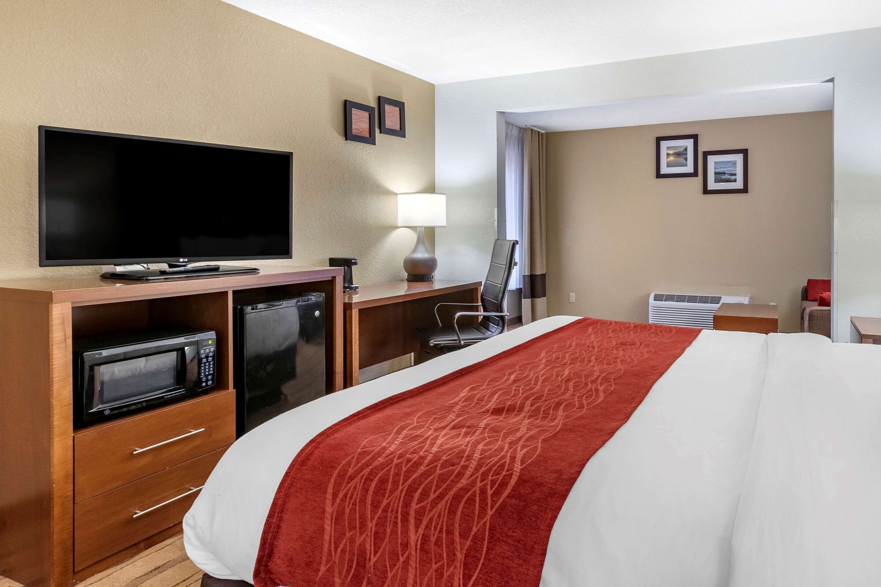 Una habitación de hotel con cama, escritorio con computadora, microondas, televisor y lámpara.