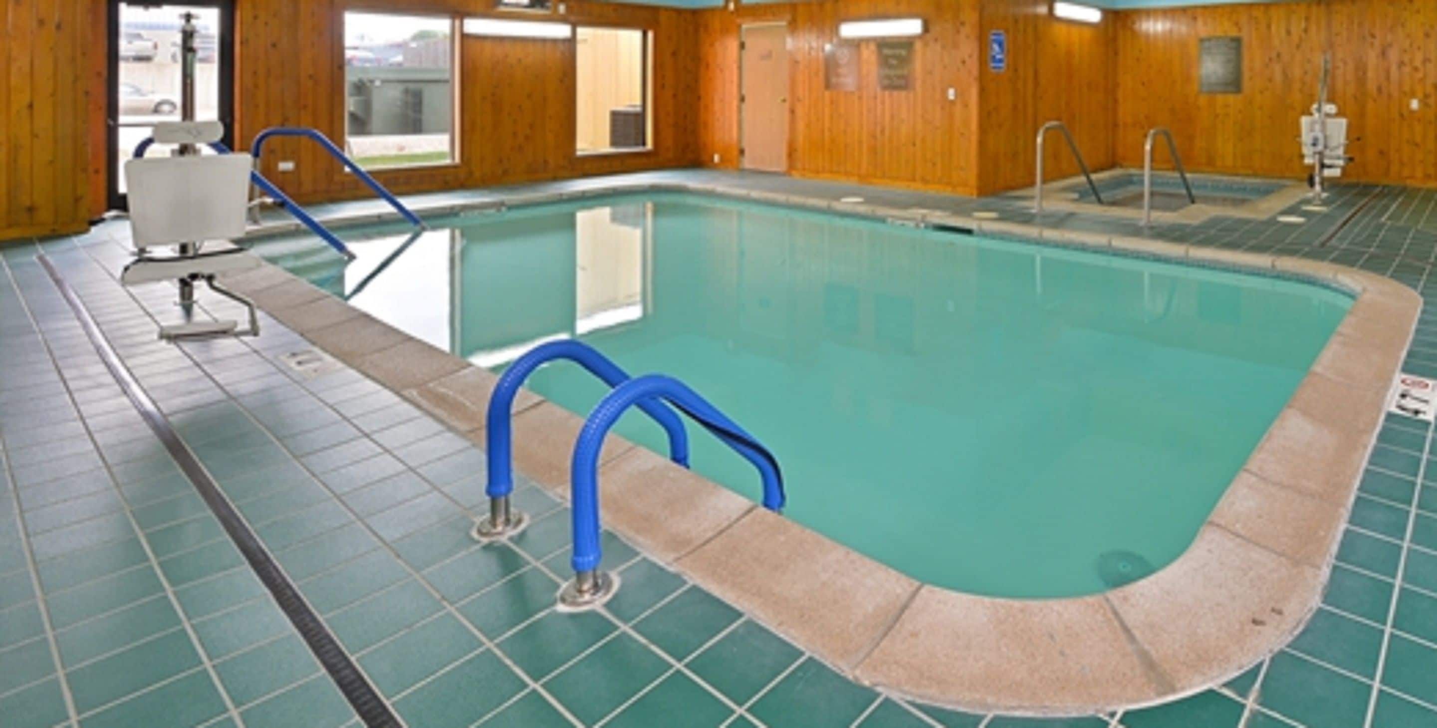 Una piscina interior con barandales de seguridad azules, suelo de baldosas y paredes de madera.