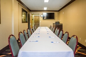 Un salón de conferencias con una larga mesa, sillas, un reloj y un televisor en la pared.