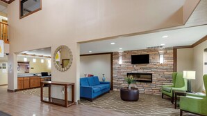 A hotel lobby with a blue sofa, green armchairs, a stone fireplace, and a flat-screen TV mounted on the wall. - Comfort Inn & Suites Cedar Rapids North - Collins Road (Cedar Rapids)