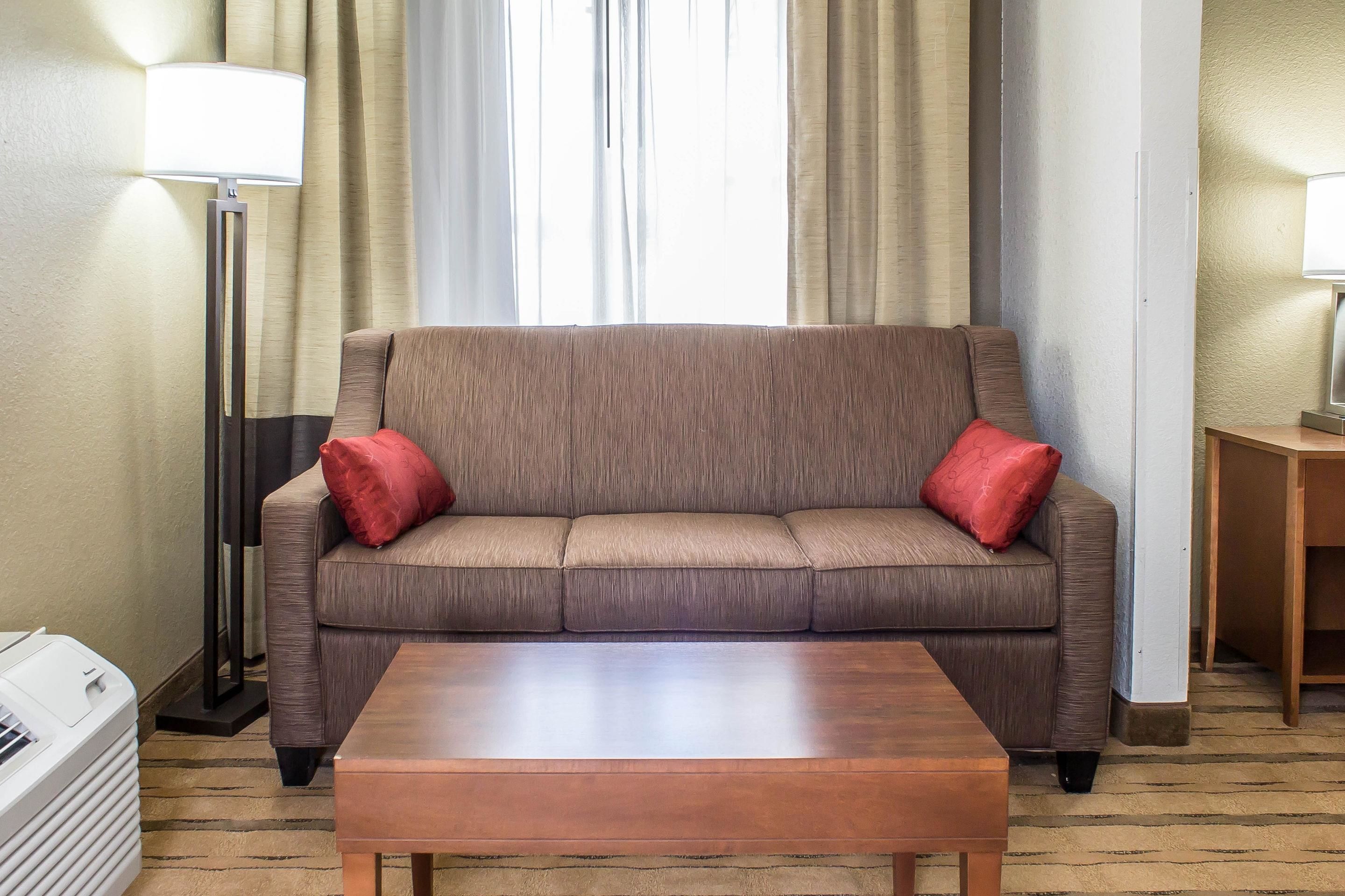 Een hotelkamer met een bruine bank, twee rode kussens, een houten salontafel, een vloerlamp en een tv-meubel.