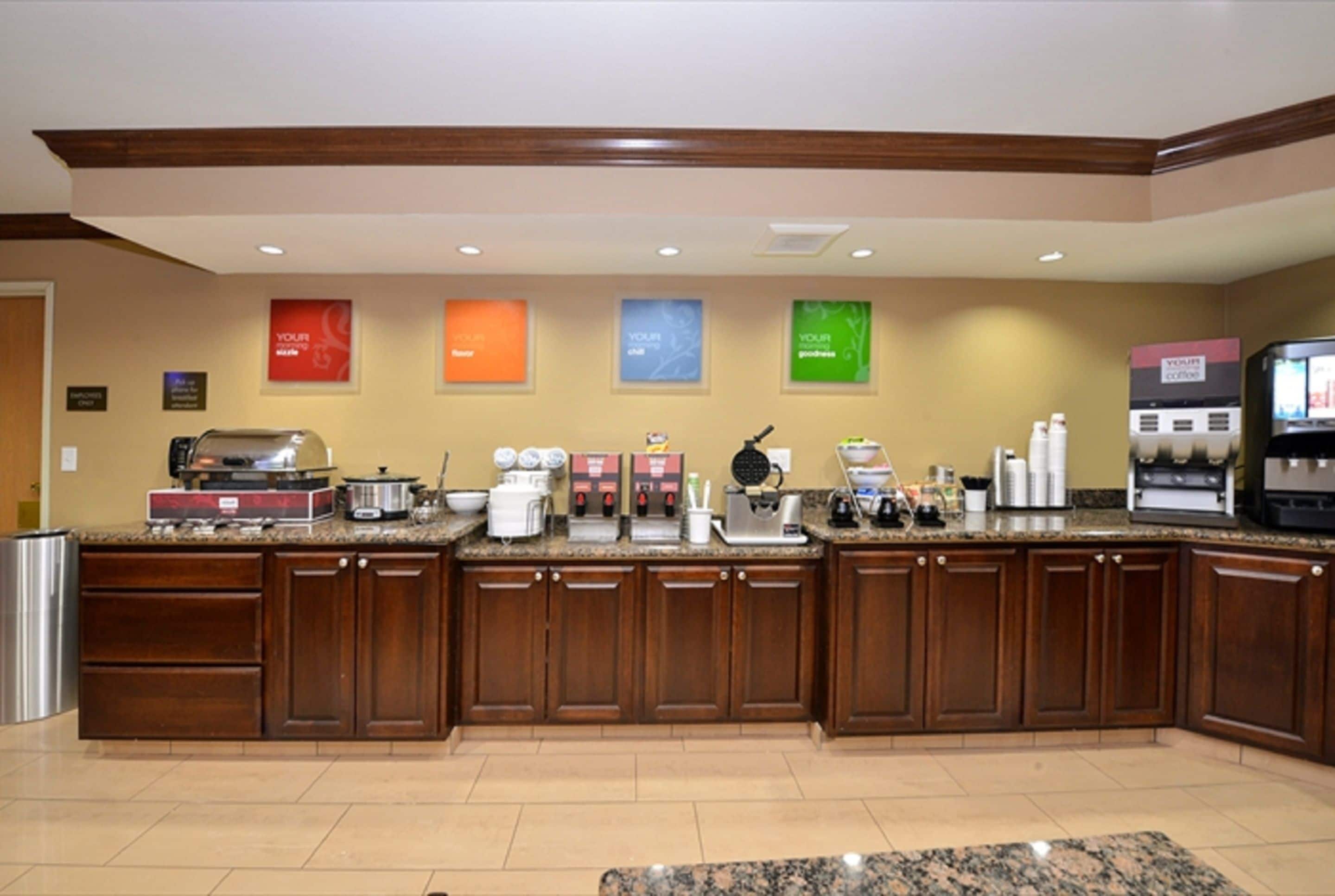A hotel kitchen with wooden cabinets, granite countertops, and various appliances including a coffee machine and a rice cooker.