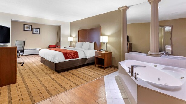A hotel room with a large bed, a desk, a chair, a desk lamp, a bedside table, a mirror, and a bathtub. - Comfort Inn & Suites Cedar Rapids North - Collins Road (Cedar Rapids)