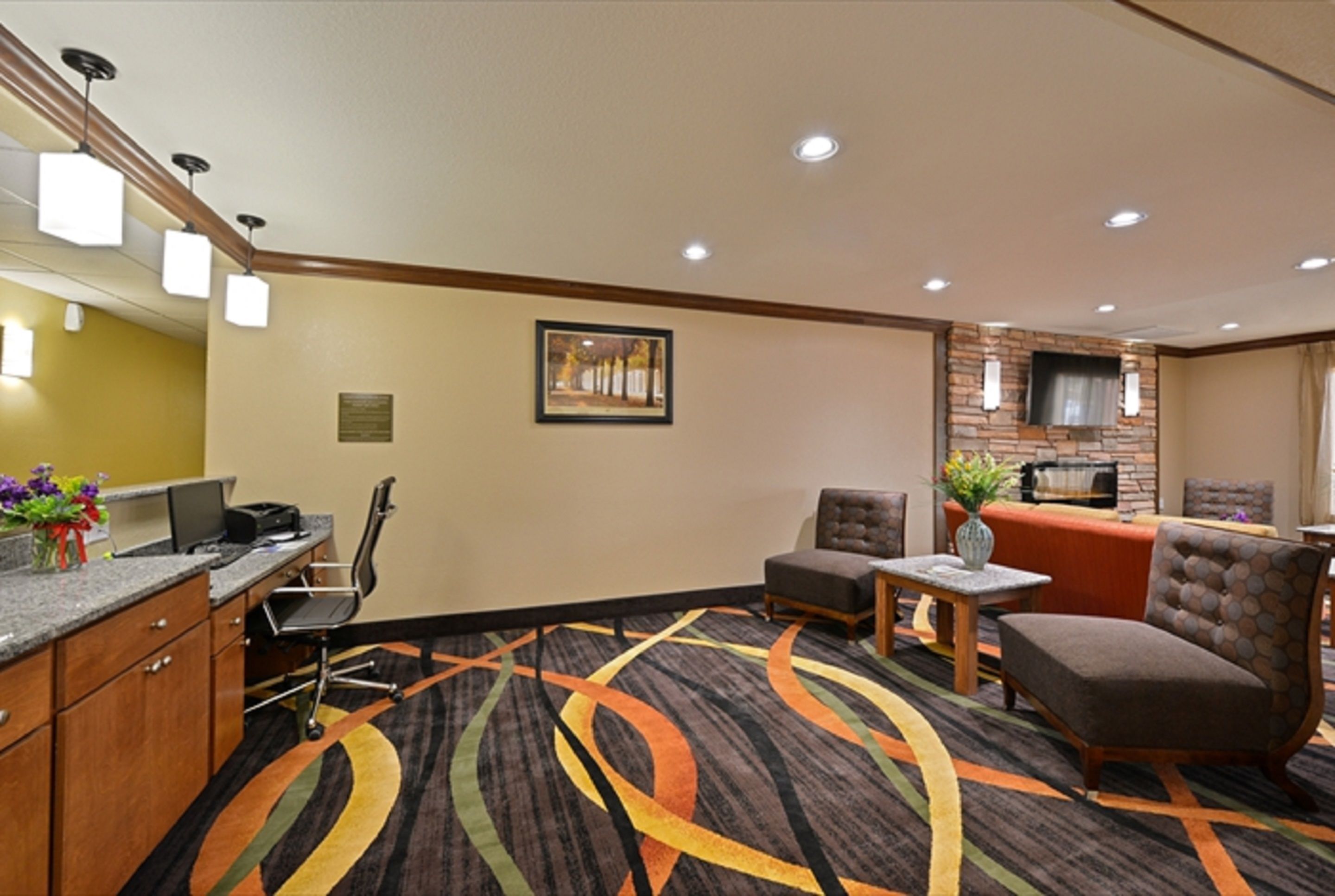 A hotel lobby with a reception desk, a seating area with chairs and a sofa, a fireplace, and a patterned carpet.