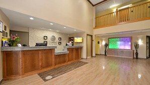 A hotel reception area with a reception desk, a large screen, and a wooden balcony. - Comfort Inn & Suites Cedar Rapids North - Collins Road (Cedar Rapids)