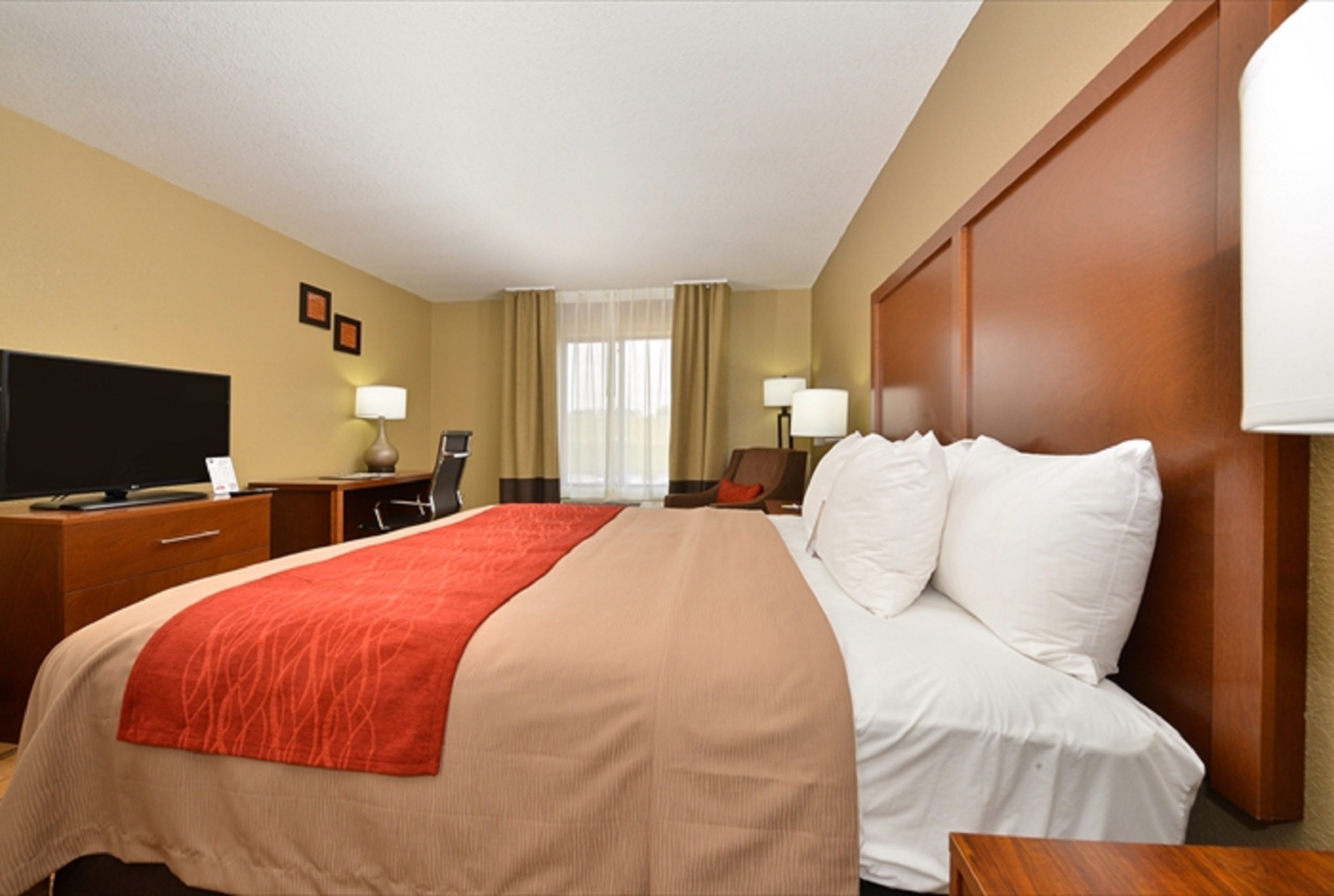 A hotel room with a bed, a desk with a computer, a TV, and a window with curtains.