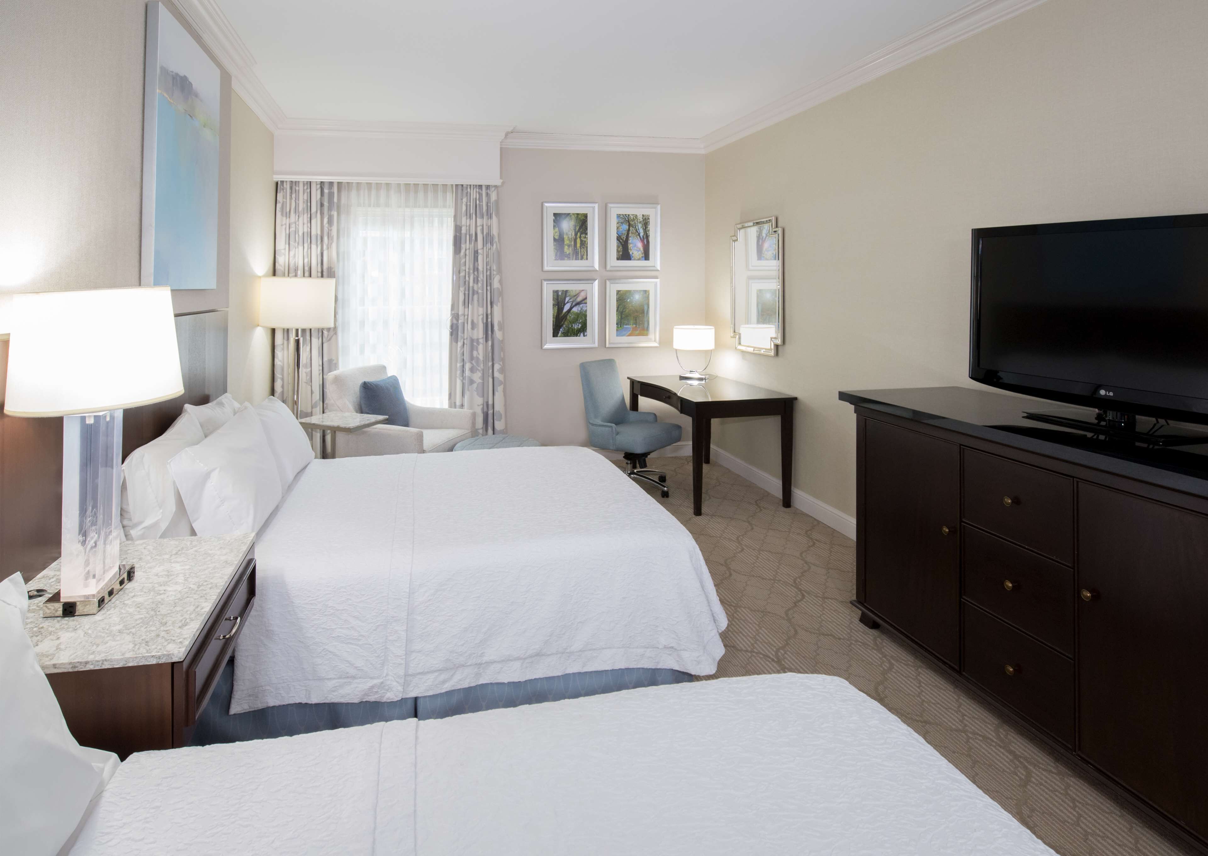 A hotel room with two beds, a desk, a TV, and a chair.