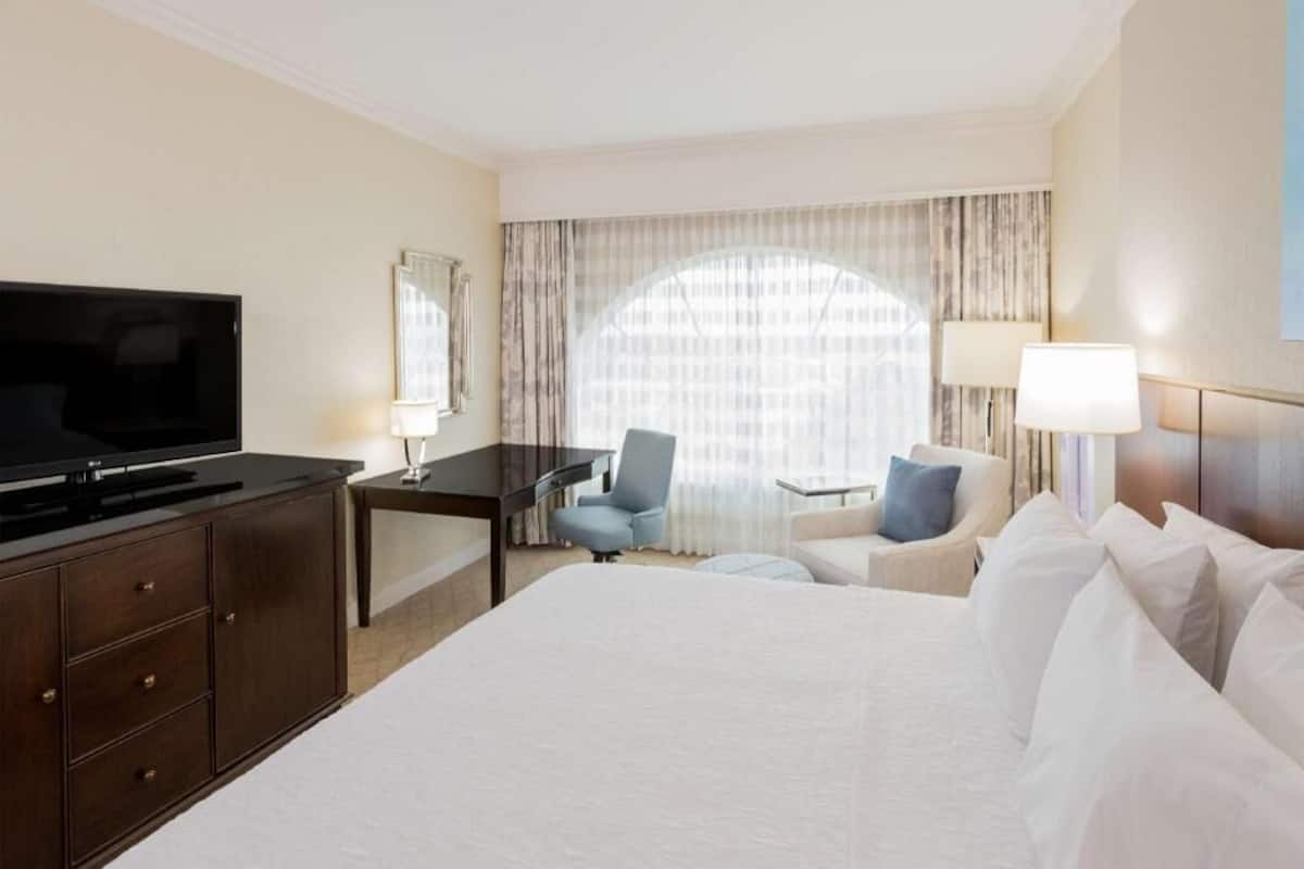 A hotel room with a bed, a desk, a chair, a TV, and a window with curtains.