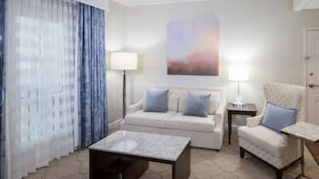 A hotel room with a sofa, armchair, coffee table, and a painting on the wall.