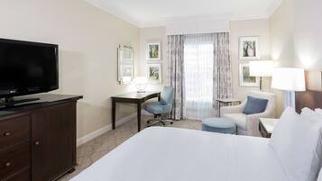 A hotel room with a large bed, a desk, a chair, a television, and a small table with a lamp.
