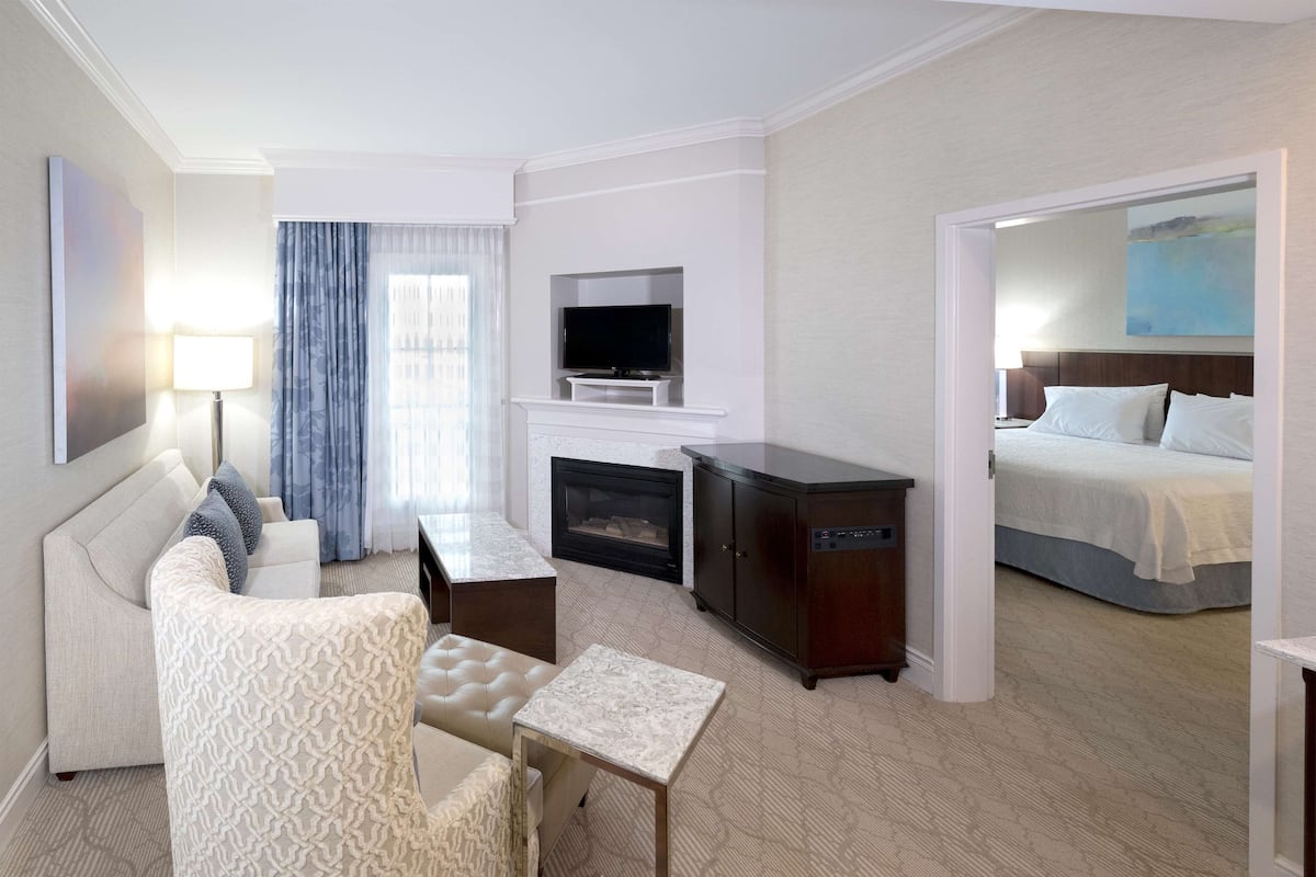 A hotel room with a sofa, a small table, a TV, a fireplace, and a bed.