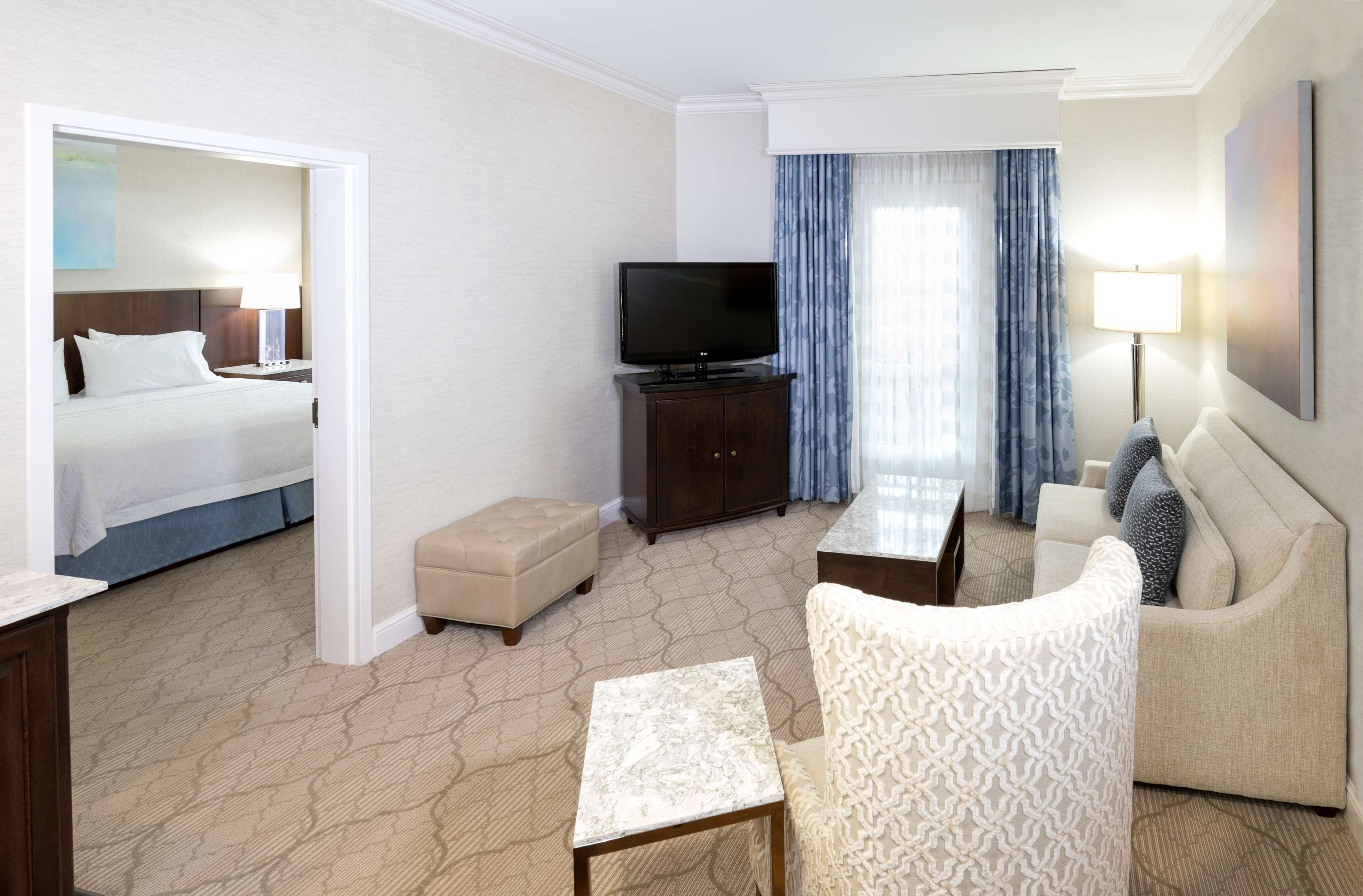 A hotel room with a bed, a television, a sofa, a small table, and a lamp.