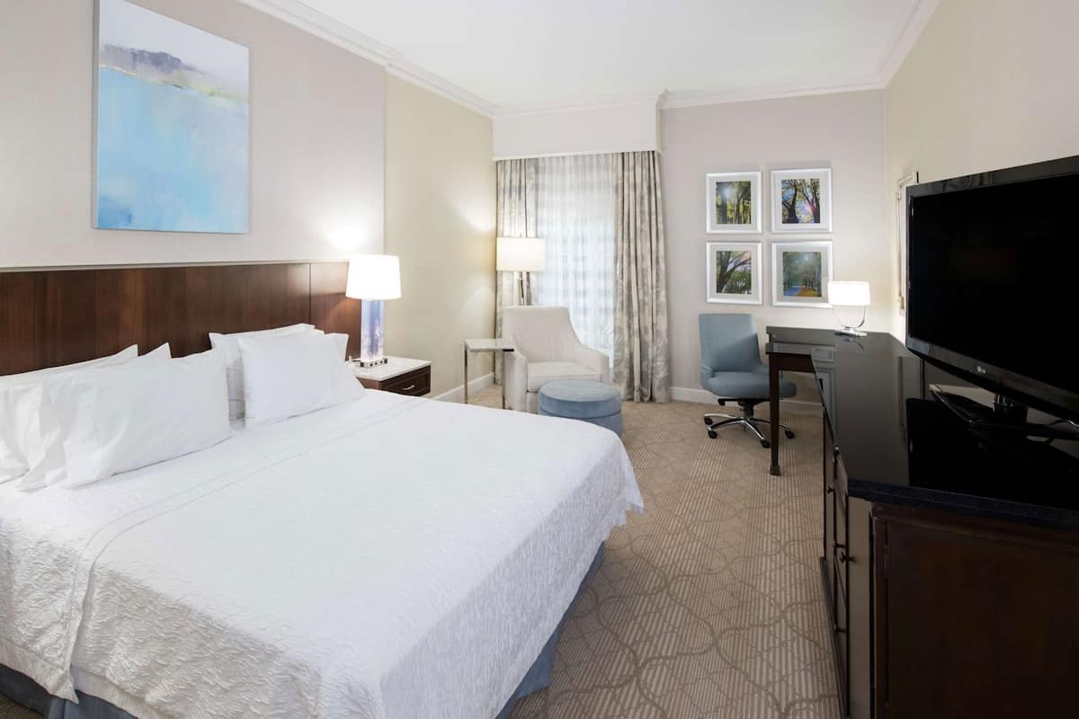 A hotel room with a large bed, a desk with a computer, a TV, and a chair.