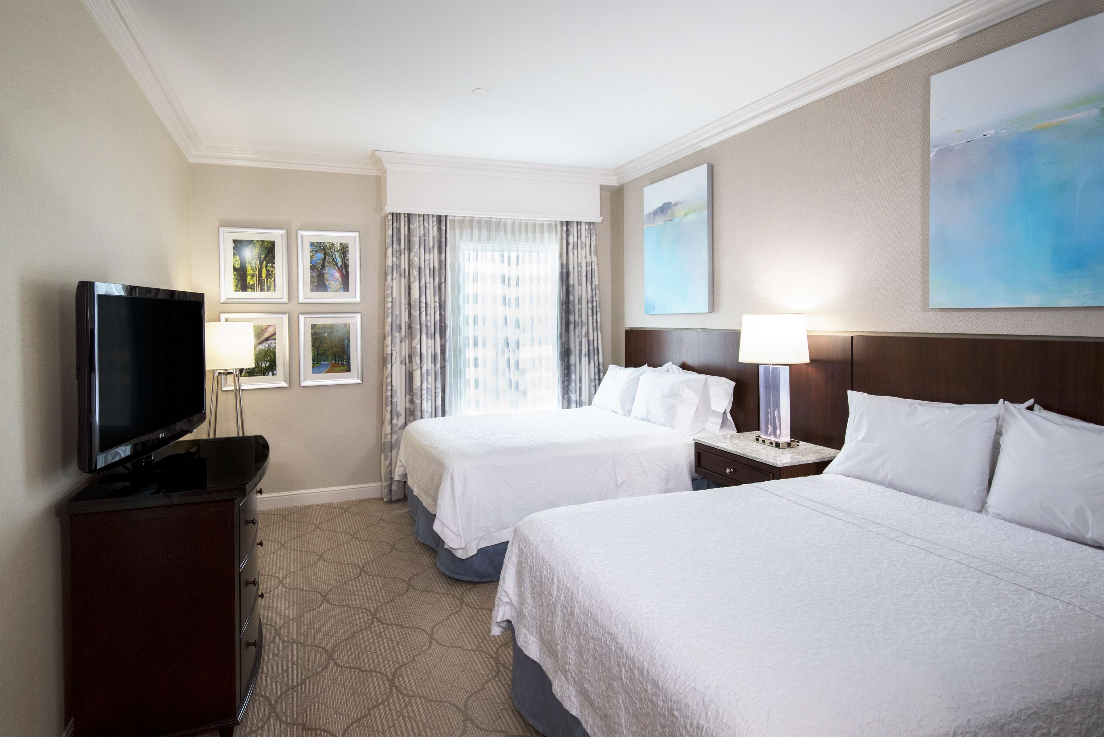 A hotel room with two beds, a TV, and a desk with a lamp.