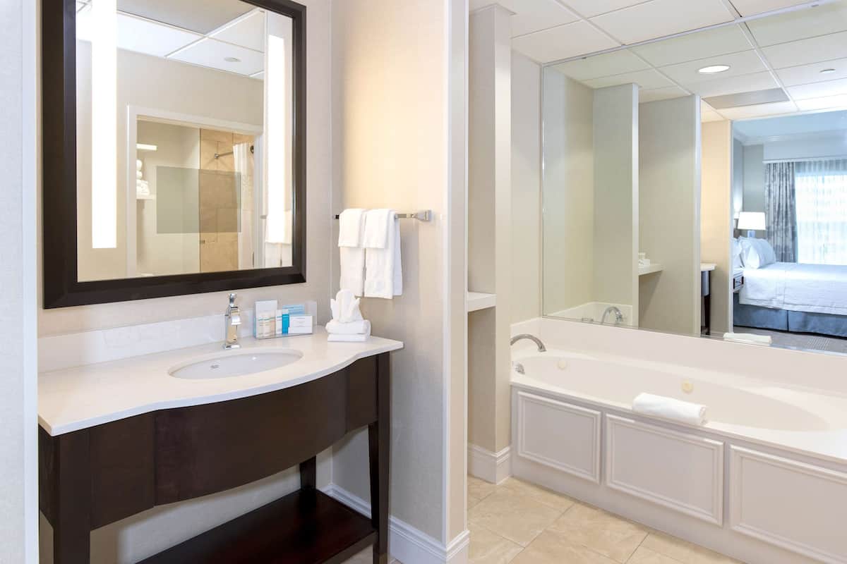 A modern bathroom with a large mirror, a sink, a bathtub, and a shower.