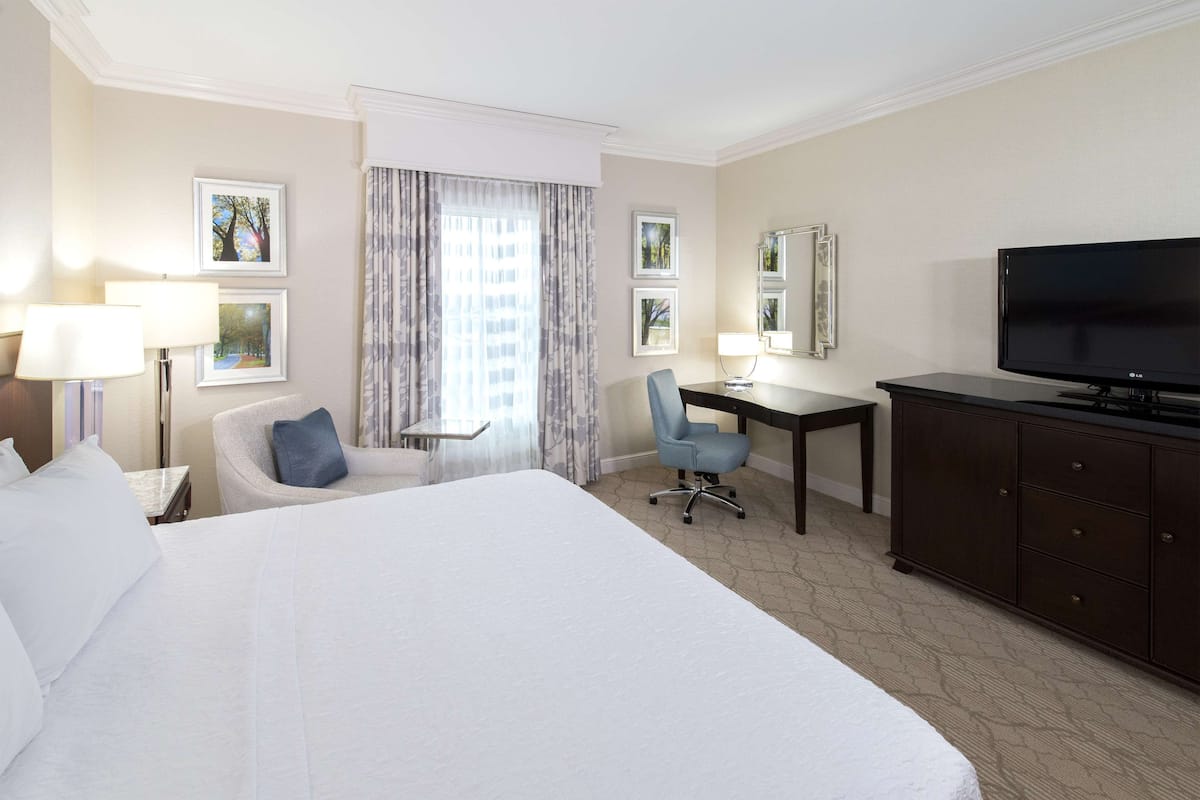 A hotel room with a large bed, a desk with a chair, a television, and framed pictures on the walls.
