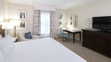 Een hotelkamer met een groot bed, een bureau met stoel, een televisie en ingelijste foto’s aan de muur.