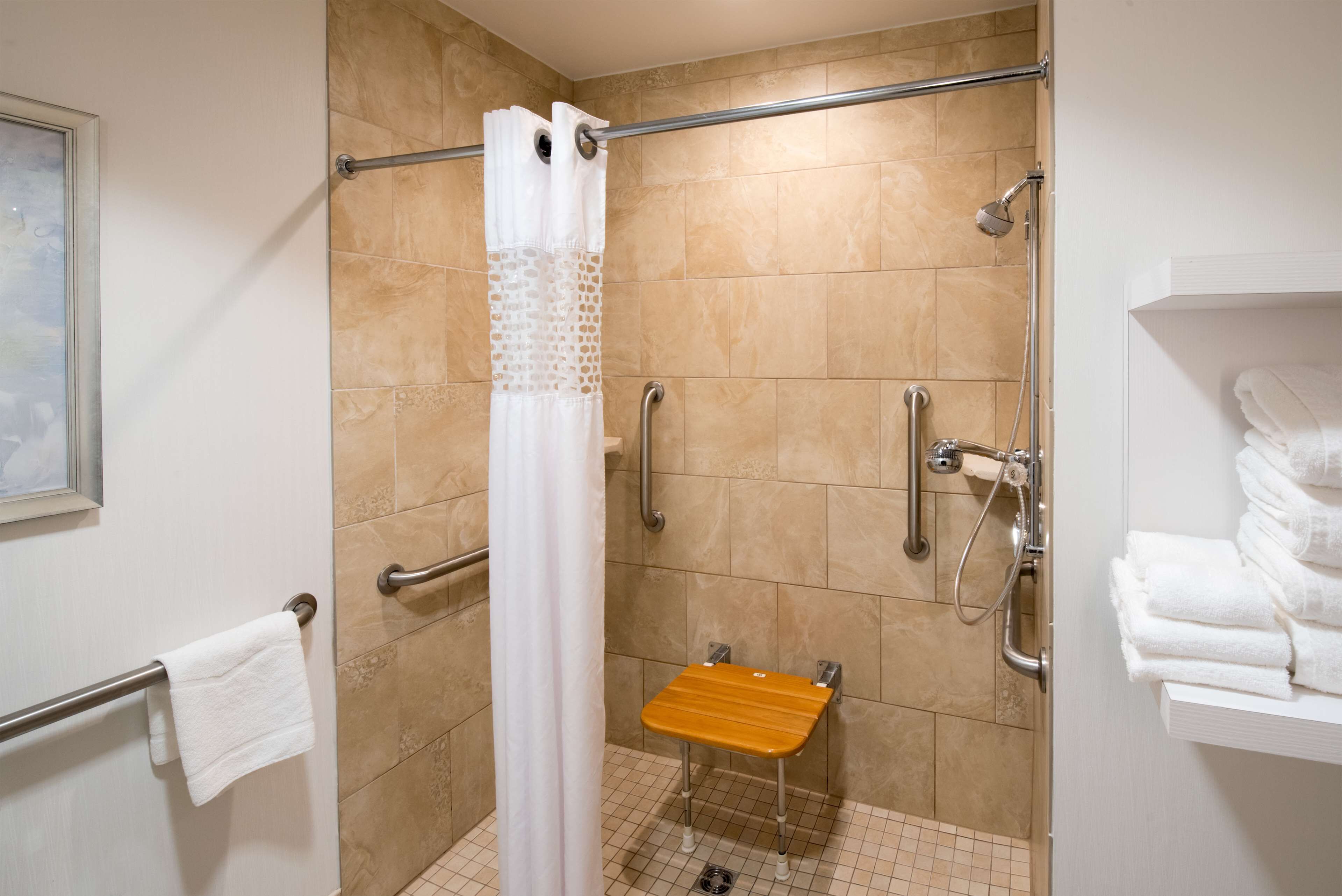A shower area with a grab bar, a wooden bench, and a white towel rack.