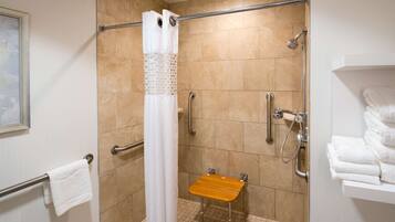 Un área de ducha con una barra de apoyo, un banco de madera y un perchero blanco.