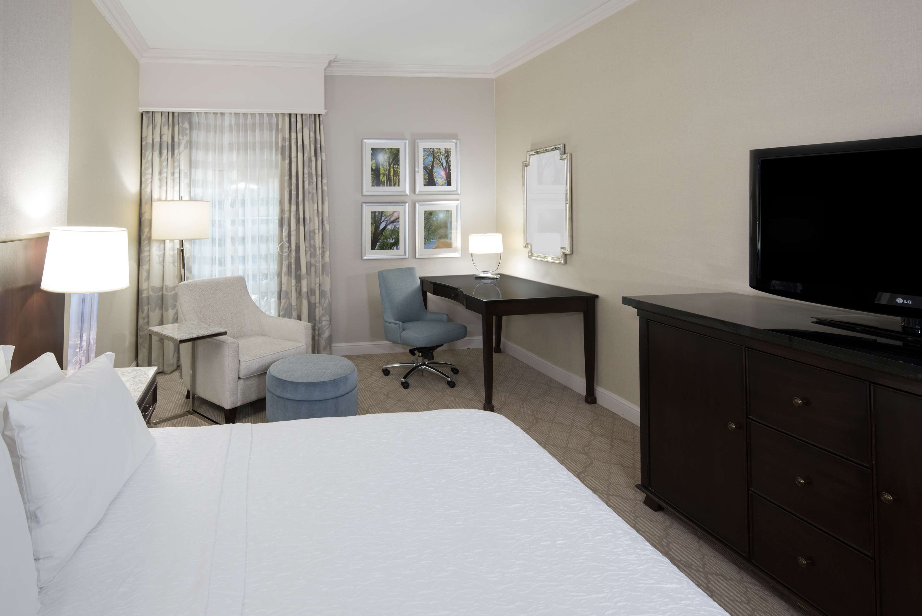 A hotel room with a bed, a desk, a chair, a television, and a wardrobe.