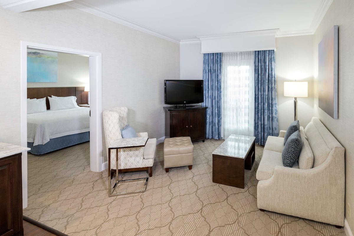 A hotel room with a bed, a TV, a sofa, a coffee table, and a chair.