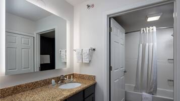 A bathroom with a granite countertop sink, a mirror, a shower with a curtain, and a toilet.