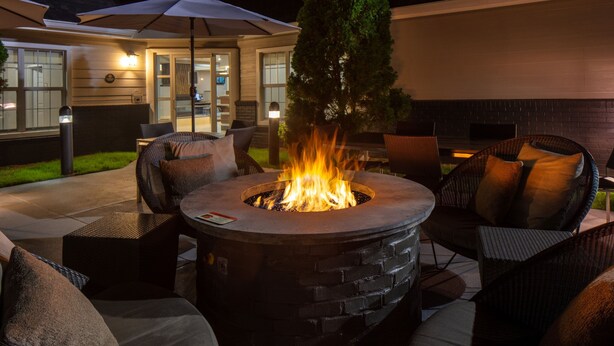 An outdoor patio with a stone fire pit surrounded by wicker furniture and a large umbrella. - Residence Inn by Marriott Little Rock (Little Rock)