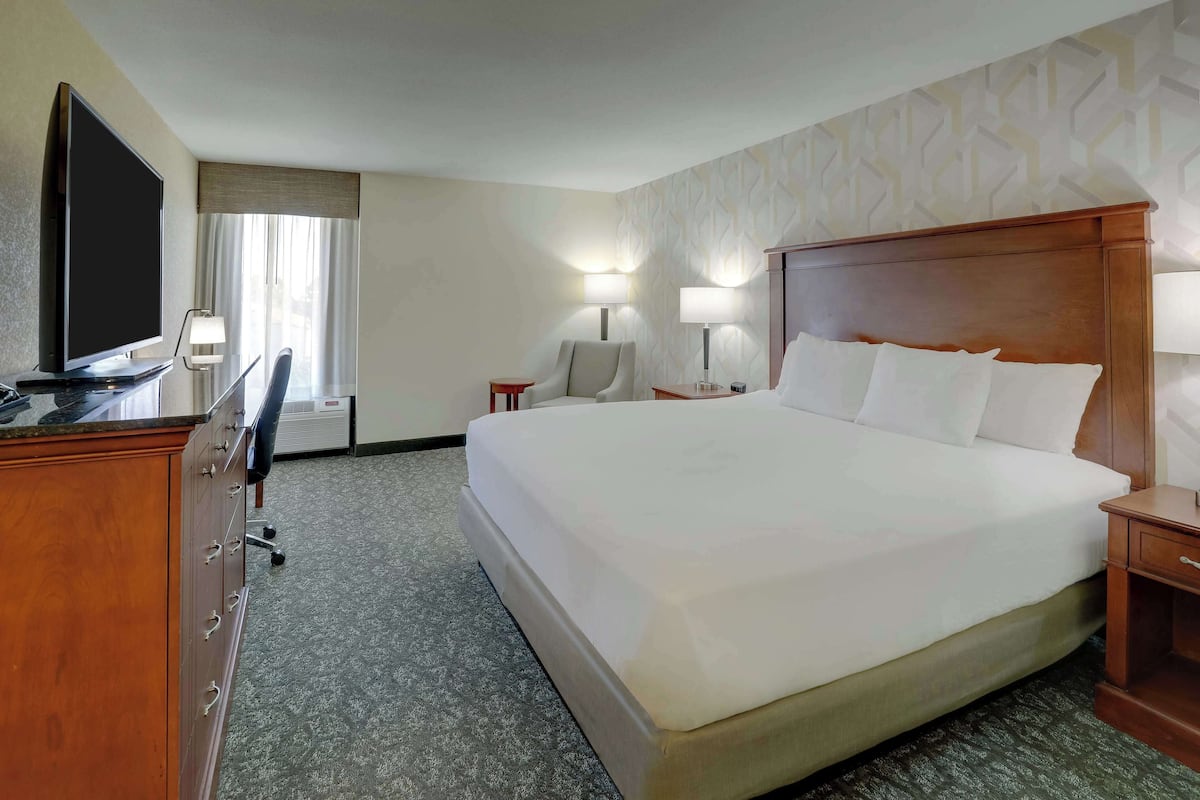 A hotel room with a large bed, a TV, a desk with a chair, and two bedside lamps.