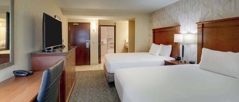 A hotel room with two beds, a desk with a chair, a TV, and a bathroom visible through an open door.