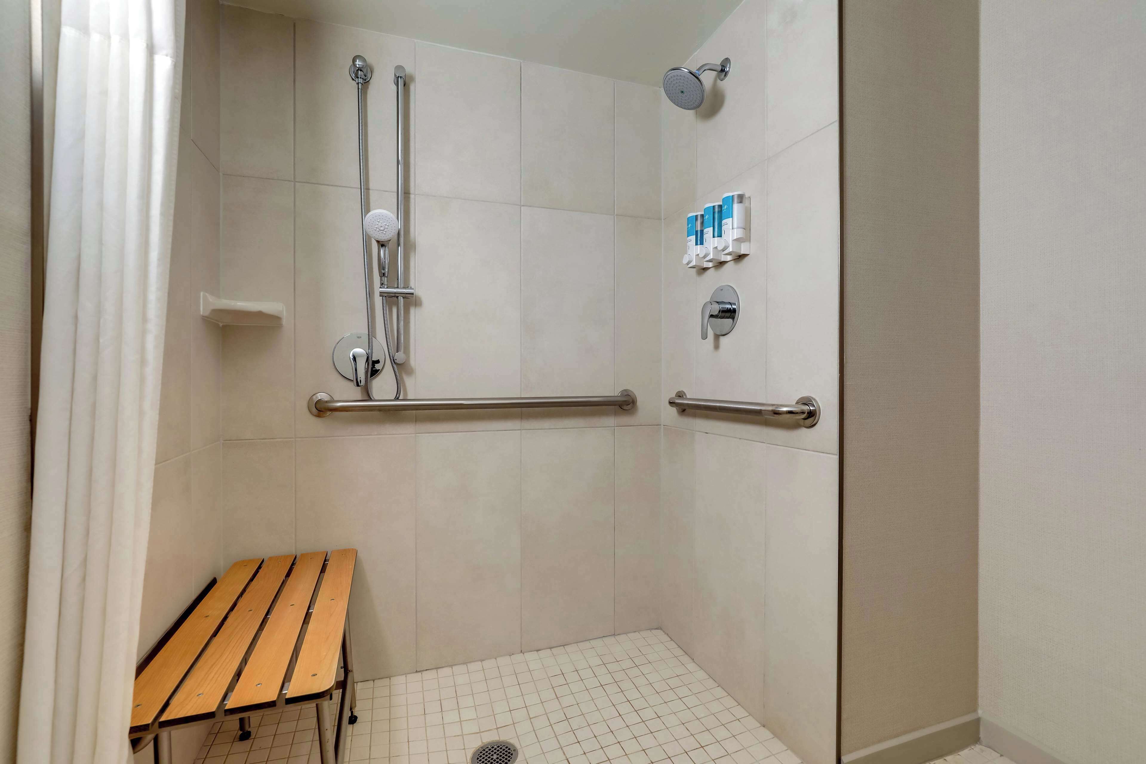 A shower area with a bench, grab bars, and a handheld showerhead.