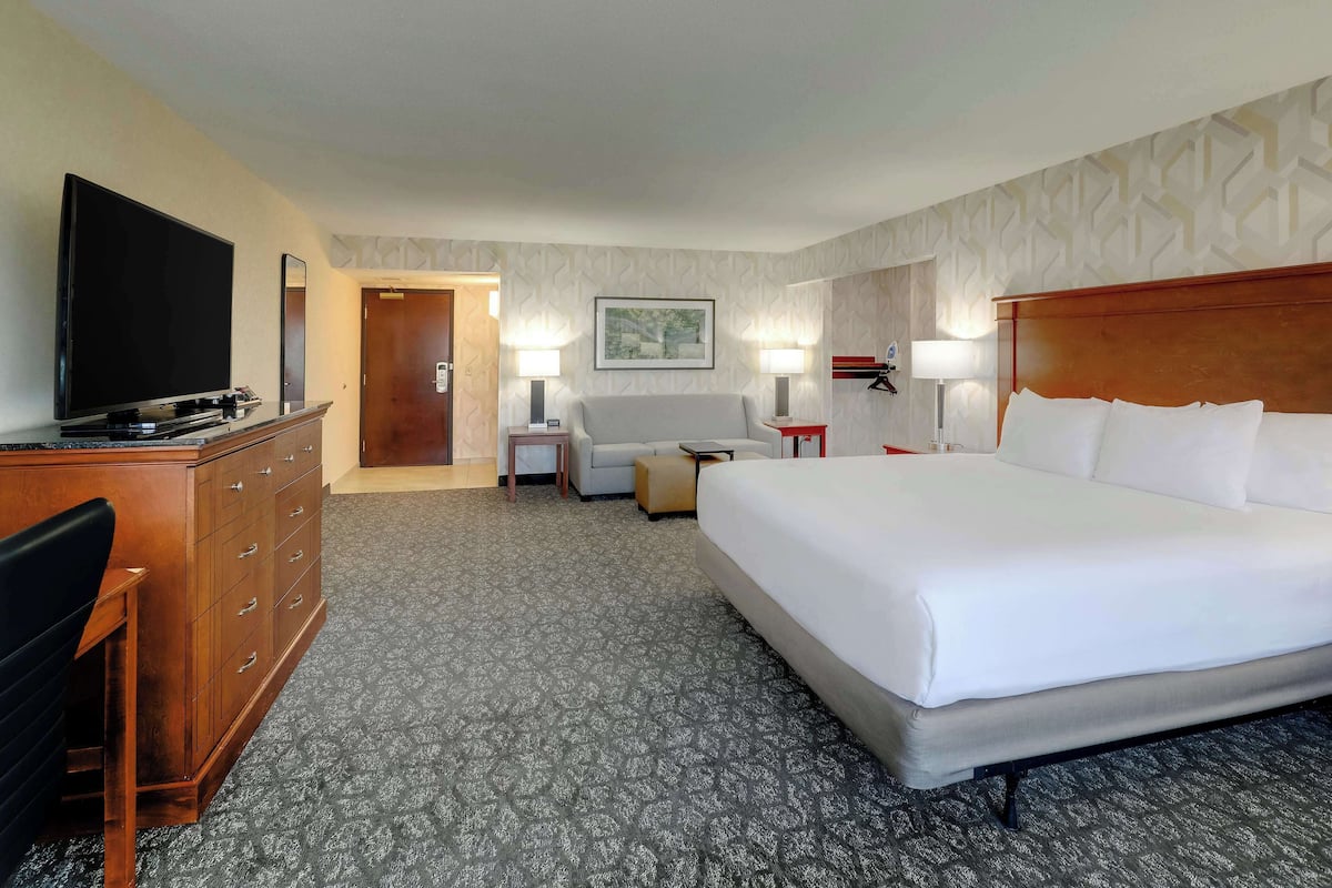 A hotel room with a large bed, a flat-screen TV, a dresser, a chair, and a desk with a lamp.