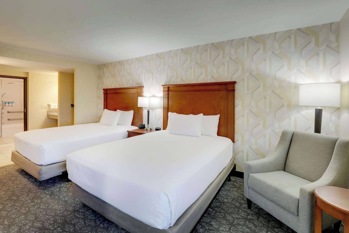 A hotel room with two beds, a sofa, and a lamp.