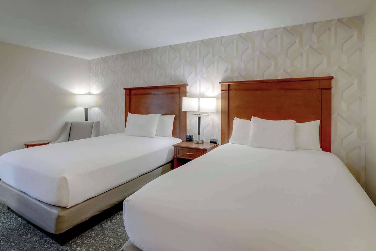 A hotel room with two beds, each with a wooden headboard, a nightstand, a lamp, and a patterned wall.