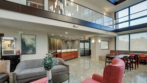 A hotel lobby with a reception desk, seating area, and a staircase to an upper level.