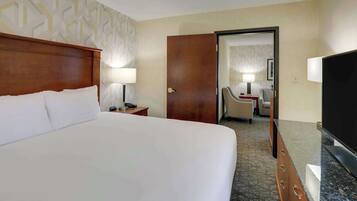 Een hotelkamer met een groot bed, een houten hoofdeinde, een nachtkastje met een lamp, een bureau met een stoel en een televisie.