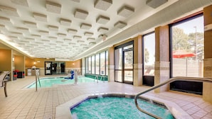 A hotel pool area with a hot tub, tiled flooring, and large windows.
