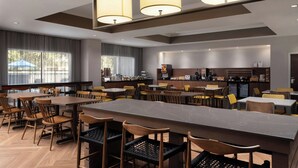 En modern hotellrestaurang med flera bord och stolar, en central bardisk och ett kök i bakgrunden.