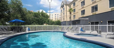 A swimming pool with lounge chairs and umbrellas, surrounded by a white fence and palm trees.