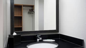 A modern bathroom with a black sink, a mirror, and a wooden shelf with hangers.