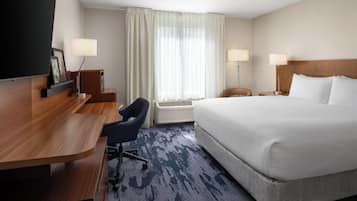Quarto de hotel com uma cama grande, uma escrivaninha com cadeira, televisão e duas luminárias de cabeceira.