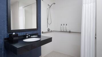 A modern bathroom with a black countertop sink, a large mirror, a shower with a handheld showerhead, and a white shower curtain.