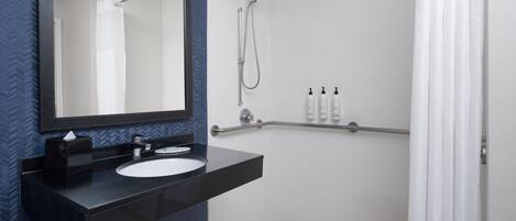 A modern bathroom with a black countertop sink, a large mirror, a shower with a handheld showerhead, and a white shower curtain.