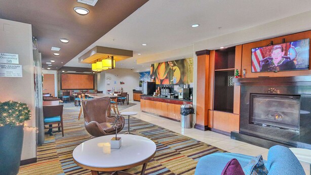 A hotel lobby with a seating area, a fireplace, a television, and a kitchen area. - Comfort Inn & Suites Houston North - Spring (Houston)