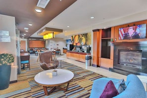 A hotel lobby with a seating area, a fireplace, a television, and a kitchen area.