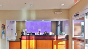 A hotel reception desk with a glass partition, a digital screen, and a small Christmas tree decoration. - Comfort Inn & Suites Houston North - Spring (Houston)