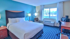 A hotel room with a bed, a desk, a chair, a lamp, an air conditioner, and a window with curtains. - Comfort Inn & Suites Houston North - Spring (Houston)