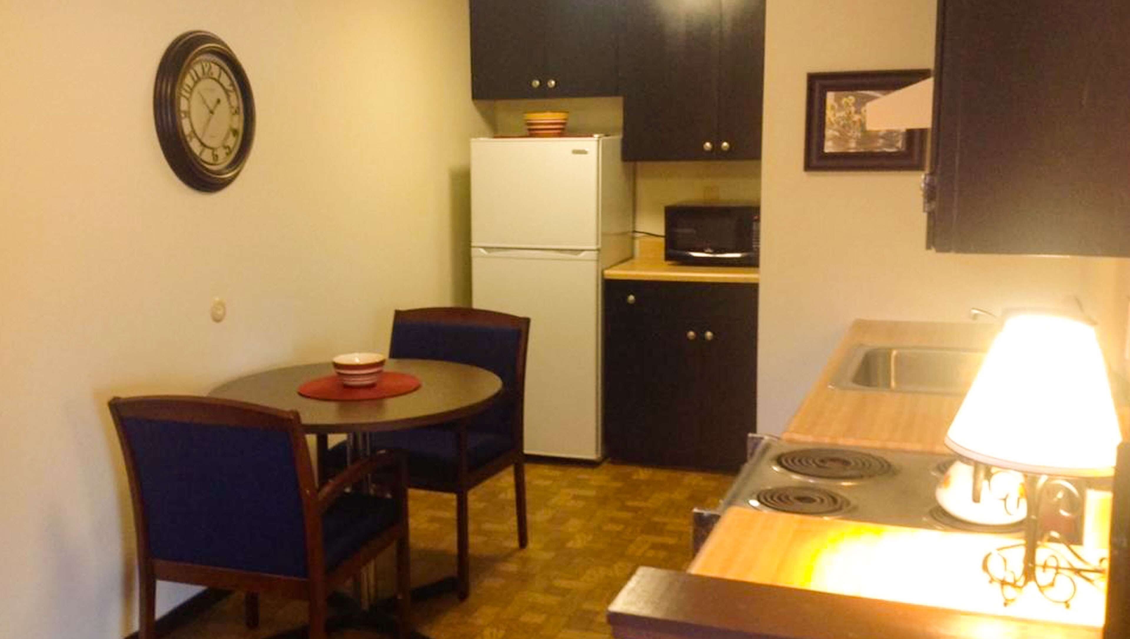 A compact kitchen with a refrigerator, microwave, stove, and a dining area with two chairs and a table.