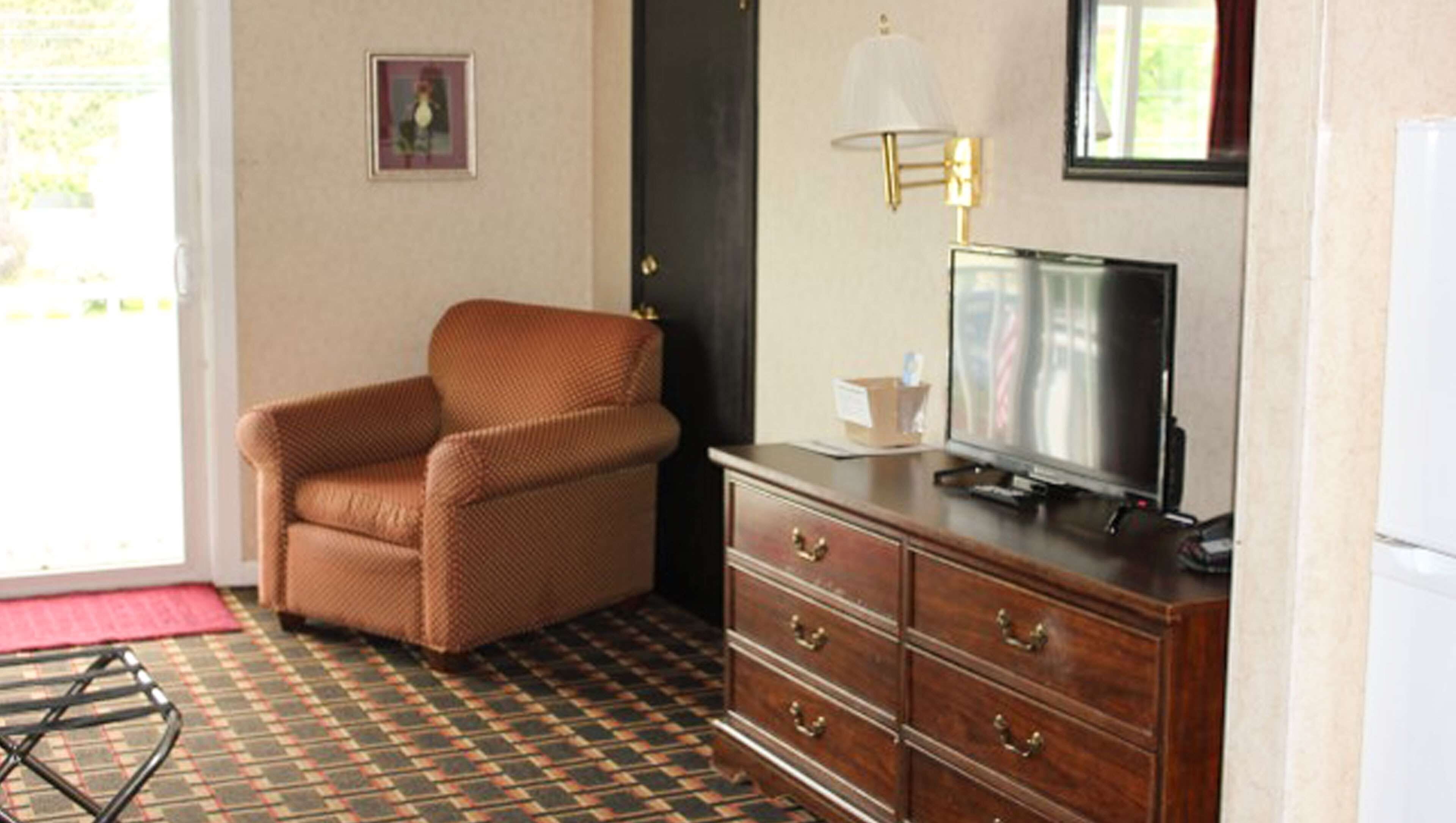 Ein Zimmer mit braunem Sessel, einer Holzkommode mit Schubladen, einem Fernseher darauf und einem gemusterten Boden.