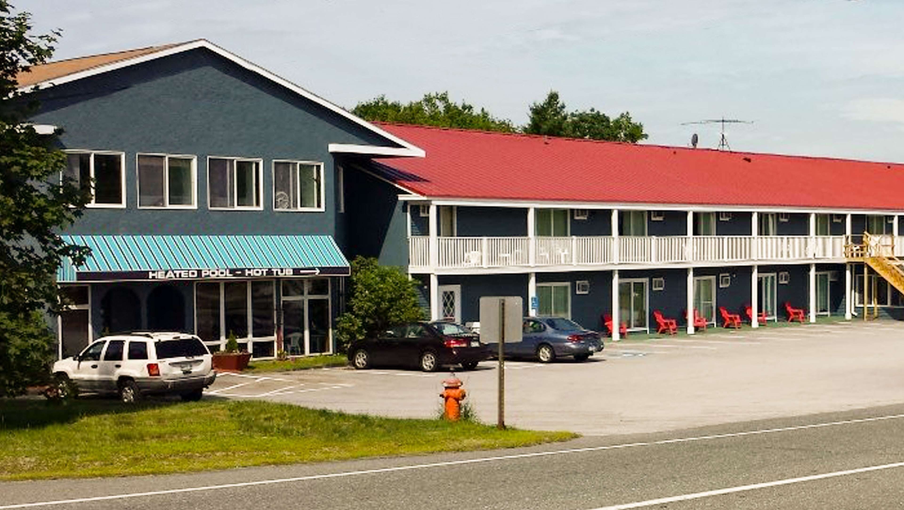 Un motel avec un toit rouge, une piscine et un panneau indiquant la présence d’une piscine chauffée et d’un jacuzzi.